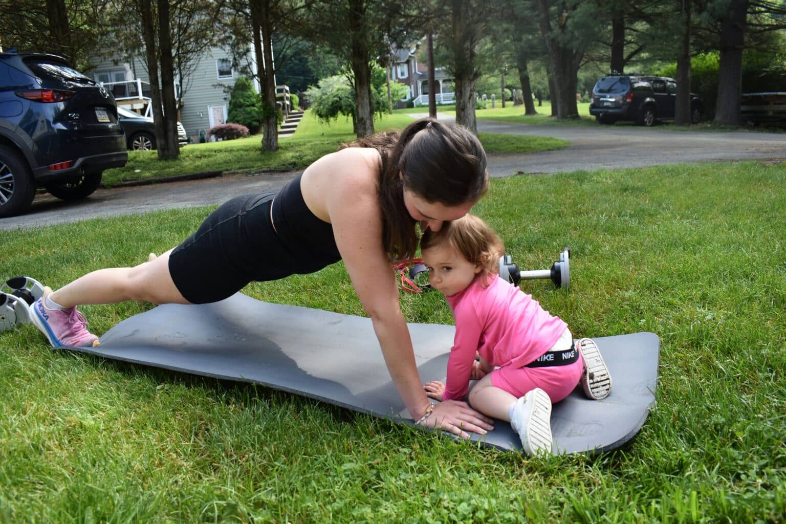 Lexi in plank position with her toddler on the workout mat — postpartum strength training, babies welcome
